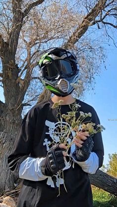 a person wearing a helmet and holding a plant in front of a tree with no leaves