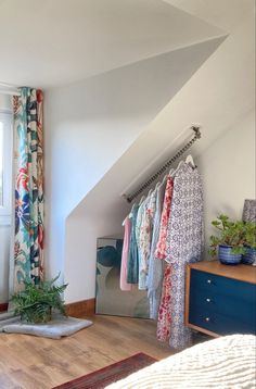 an attic bedroom with clothes hanging on the rack