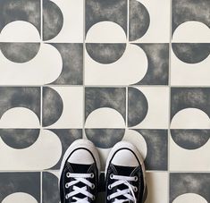 a pair of black and white sneakers on top of a tile floor next to a wall