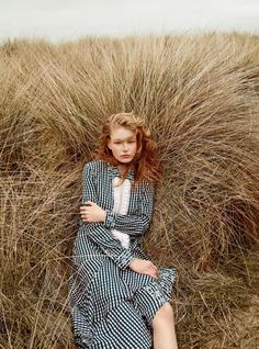 a woman sitting on top of a tall grass covered field with her legs crossed in the air