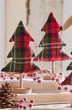 three wooden christmas trees sitting on top of a table next to pine cones and berries