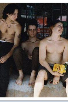 four young men sitting on steps in front of a window with no shirt on, one man holding a book and the other looking up