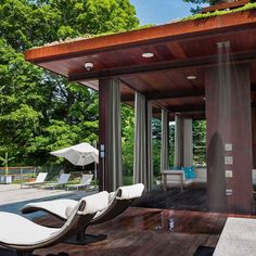 an outdoor covered patio with chaise lounges and trees in the backgroud