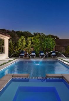 an empty swimming pool in the middle of a backyard with lounge chairs and water spouting