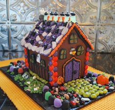 a house made out of candy on top of a black plate with orange and purple decorations