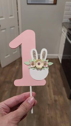 a hand holding up a pink number one cake topper