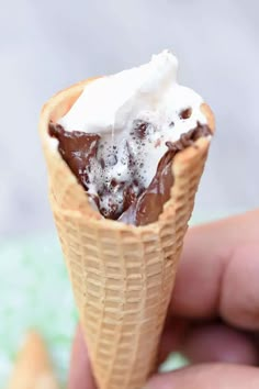 a hand holding an ice cream cone with chocolate and whipped cream in it's center