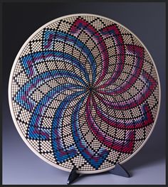 a decorative plate with blue, red and pink designs on it's side sitting on a black stand