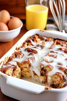 a casserole dish with white icing and cinnamon rolls in it on a wooden table