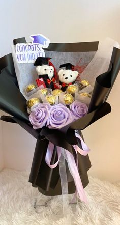 a bouquet of flowers with teddy bears and chocolates wrapped in black paper on a white furnishing