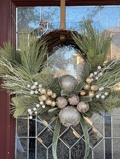 a christmas wreath hanging on the front door with pine cones and silver baubies