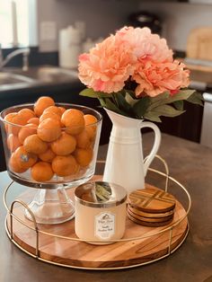 a glass bowl filled with oranges sitting on top of a wooden tray next to a vase