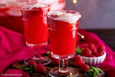 two glasses filled with liquid sitting on top of a wooden tray next to strawberries