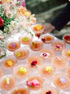 there are many small cups with flowers in them on the table and one is filled with drinks