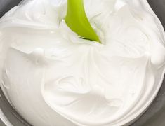 a green spatula in a metal bowl filled with white icing and whipped cream