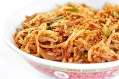 a close up of a bowl of food with noodle and vegetables in it on a white surface