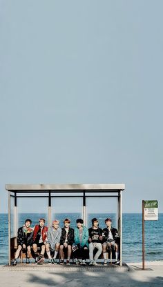 a group of people sitting on top of a bus stop next to the ocean and a sign