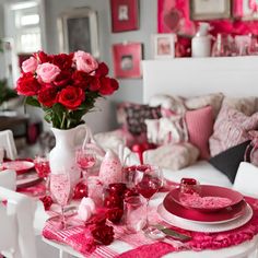 a white table topped with pink and red plates next to a vase filled with flowers