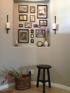 a wall with pictures on it and a stool in the corner next to some flowers