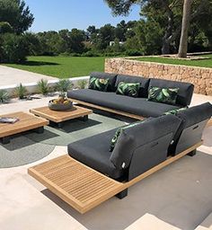 an outdoor living area with black couches and coffee table on concrete flooring, surrounded by greenery