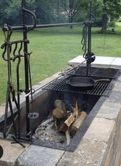 an outdoor fire pit made out of concrete blocks and steel bars with grilling tools on top