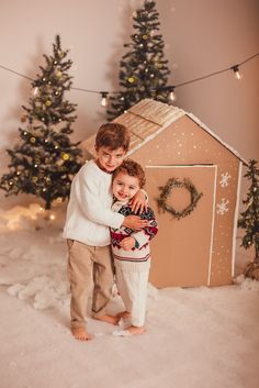 two children standing in front of a gingerbread house with christmas lights on the trees