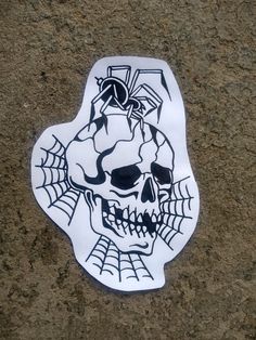 a white sticker with a skull and spider web on it's face is laying on the ground