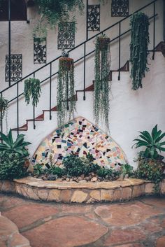 an artisticly designed fountain in front of a white building with plants growing on it