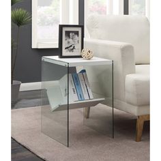 a glass side table with books on it in front of a white chair and window