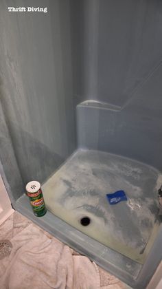 a bathroom with a shower stall and toilet paper on the floor, next to a can of paint