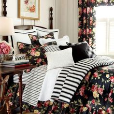 a bed covered in black and white sheets with flowers on the comforter next to a window