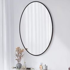 a round mirror is hanging on the wall above a white table with vases and flowers