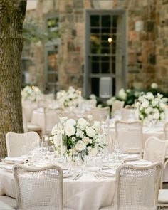 the tables are set with white flowers and place settings for an elegant wedding reception in front of a stone building