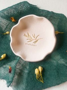 a white bowl sitting on top of a green leaf covered table cloth next to dried flowers