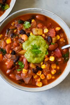 two white bowls filled with mexican soup and garnished with cilantro, black beans, avocado and corn