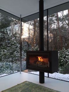 a fire place in the middle of a room with snow on the ground and trees outside