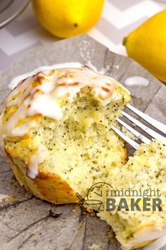 a close up of a muffin on a plate with a fork and lemons in the background