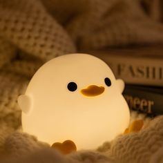 a small light that looks like a ducky is sitting on a bed next to a book