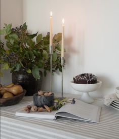 an open book sitting on top of a table next to a bowl of fruit and two candles