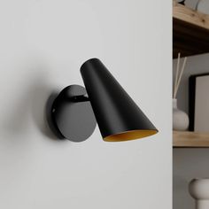 a black wall light mounted on the side of a white wall next to a shelf