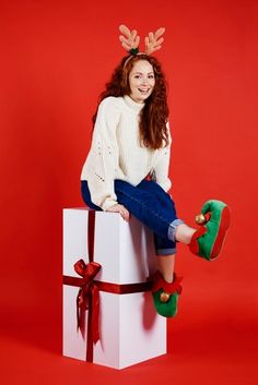 a woman sitting on top of a white present box with reindeer antlers on her head