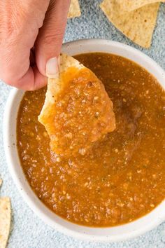 a person dipping tortilla chips into a bowl of salsa