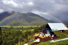 a rainbow is seen in the sky over a small cabin on a hill with trees and grass