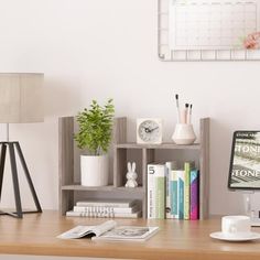 a desk with a computer monitor, books and other items on it in front of a white wall