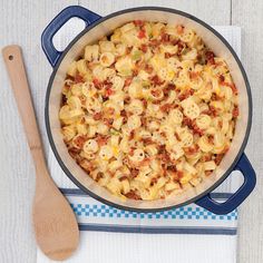 a pot filled with macaroni and cheese next to a wooden spoon on top of a white table