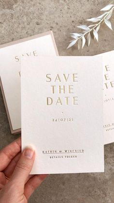 two white save the date cards with gold foil on them, held up by someone's hand