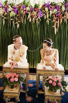 a man and woman sitting next to each other on chairs in front of a flower wall