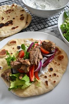 two pita breads with meat and veggies on them next to a bowl of salad