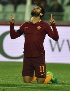 a man sitting on top of a soccer field holding his hands up in the air