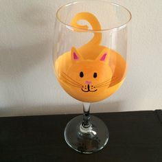 a yellow cat shaped wine glass sitting on top of a wooden table next to a white wall